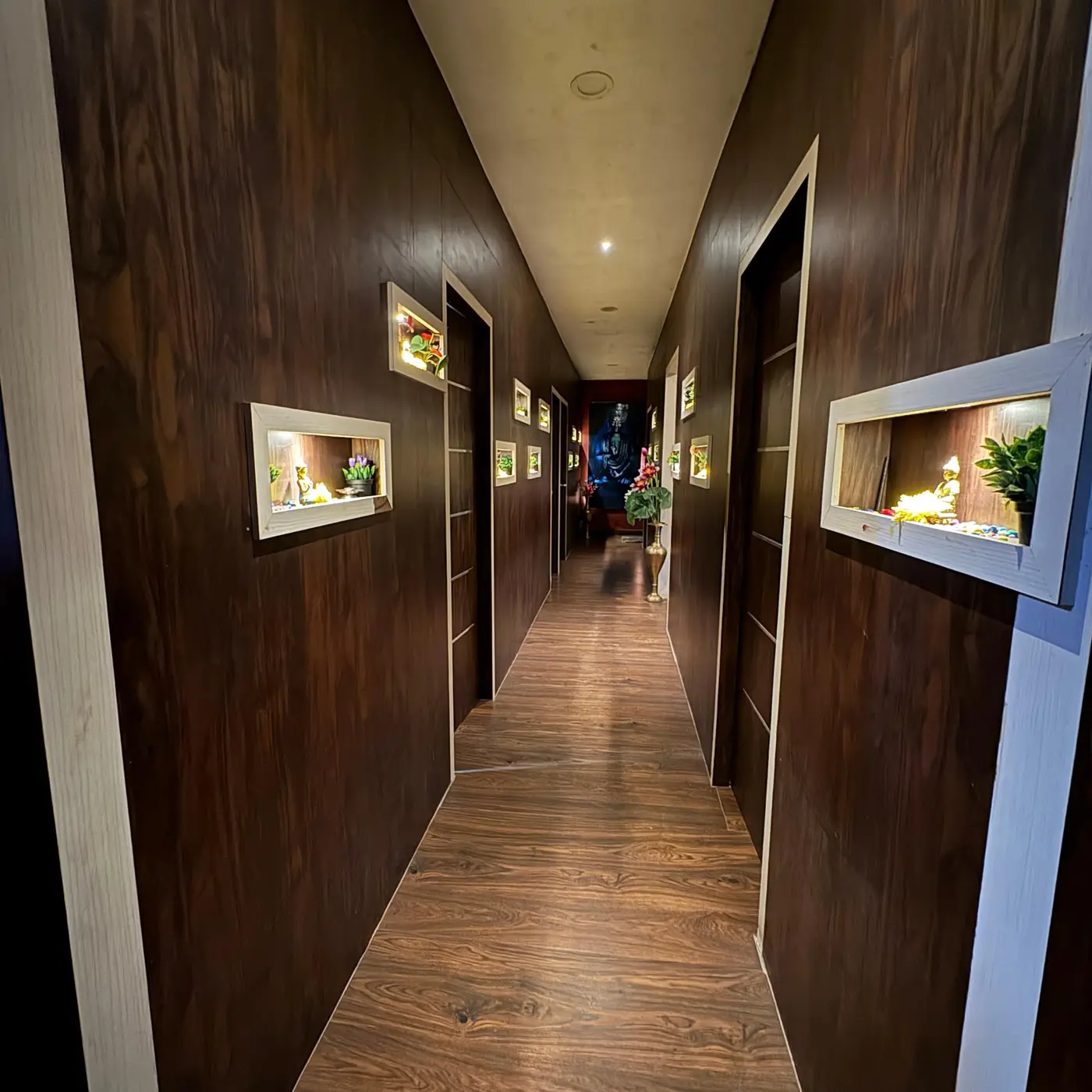 Dark wood spa corridor with illuminated niches and Buddha statues at Ocean Leaf Premium Spa