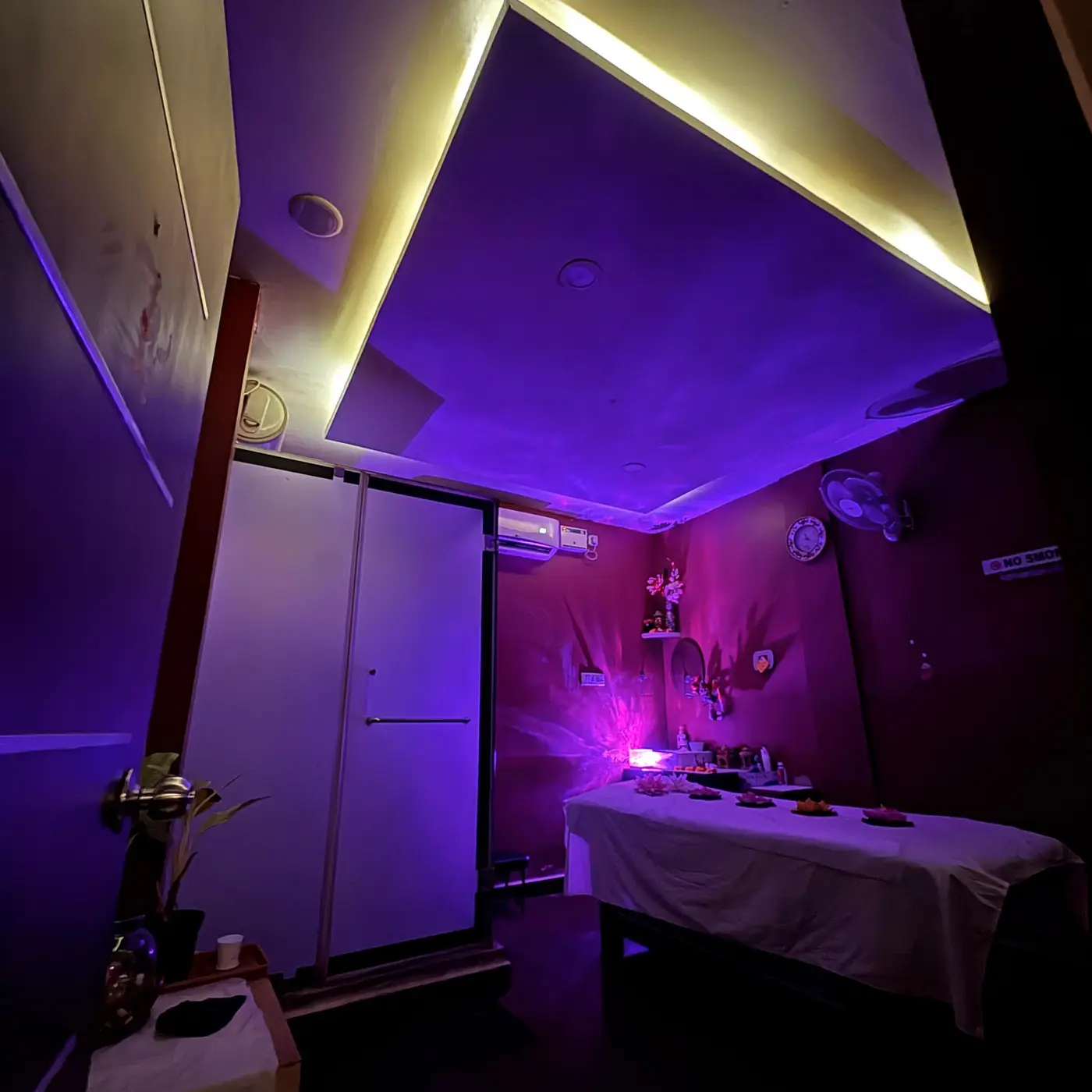 Private treatment suite with violet ambient lighting, massage bed and en-suite shower